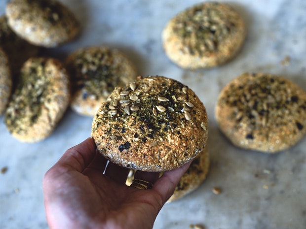 Bread in a roll shape topped with seeds held in the palm of a hand