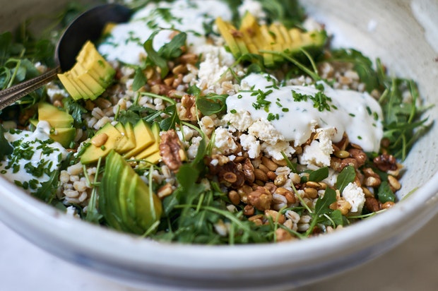 big salad bowl filled with barley, cheese, avocado, walnuts and a yogurt dressing