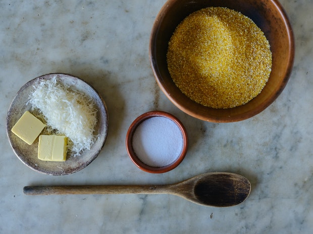 ingredients for making polenta on a counter including cornmeal, butter, grated parmesan