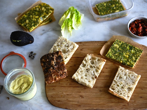 ingredients for frittata sandwiches on kitchen counter including eggs, tomatoes, aioli, lettuces