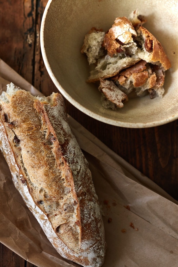 half a baguette on a paper bag alongside some torn baguette in a bowl