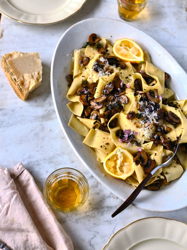 Homemade Pappardelle on a platter with sliced mushrooms and lemon