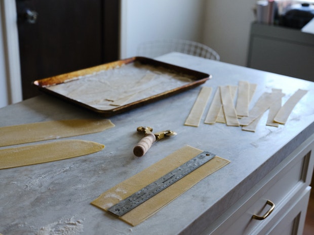 Cutting homemade pappardelle on marble countertop using ruler as a guide
