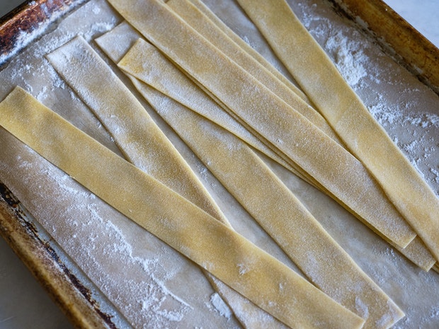 Fresh Homemade Pappardelle Noodles drying a bit on a floured sheet pan