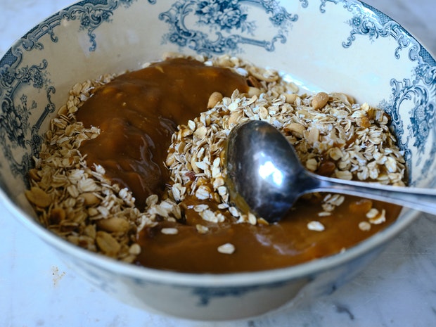 a mixing bowl filled with granola ingredients and a large spoon