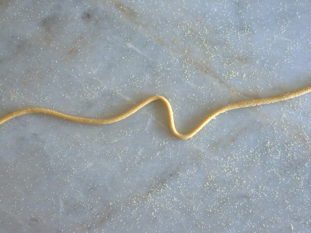 A single strand of pici on a marble countertop