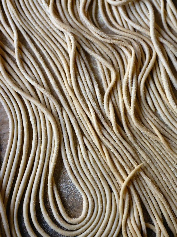Strands of pici pasta on an baking sheet