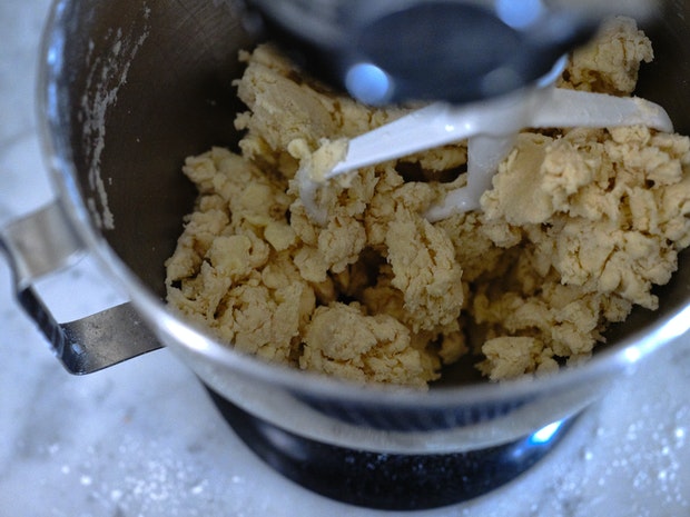 pie dough coming together in the the bowl of an electric mixer with paddle attachment
