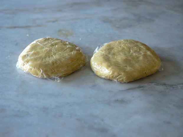 two discs of pie dough wrapped in plastic wrap