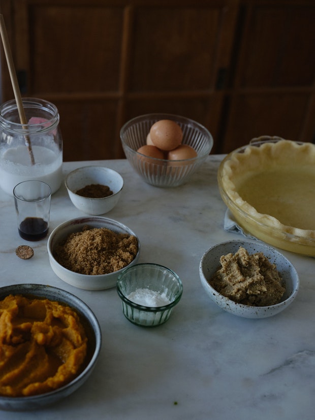 ingredients to make a pumpkin pie arranged on counter including eggs, brown sugar, pumpkin puree, and vanilla