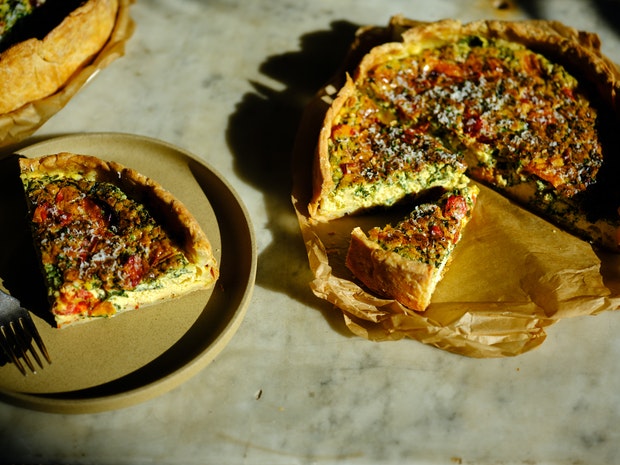 A quiche on a marble counter alongside a wedge of quiche on a plate with a fork
